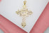 An ornate gold cross pendant rests on a white display surface, showcasing intricate filigree details and a textured center sunburst design.