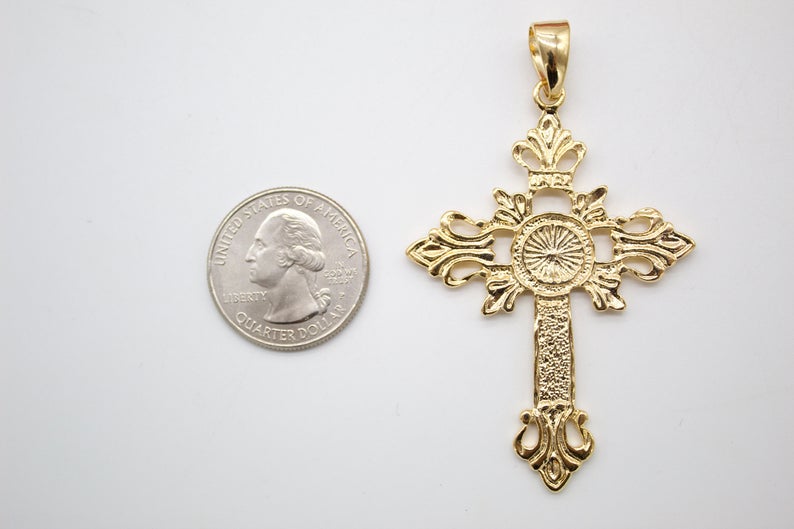 An ornate gold cross pendant rests beside a US quarter coin to show its scale.
