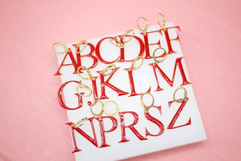 A collection of red enamel initial letter earrings with gold hoops rests neatly on a white display block.