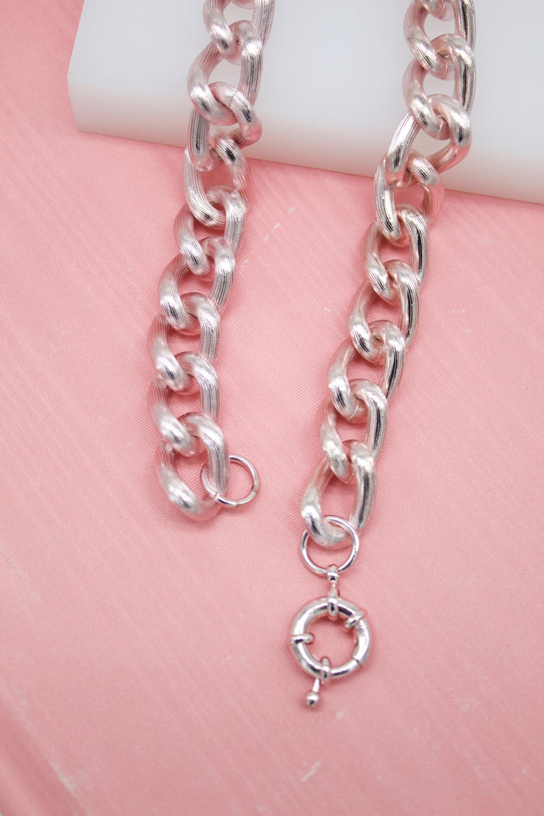 A textured silver chain necklace rests against a soft pink background.