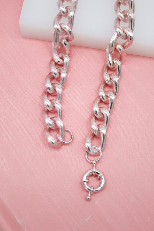 A textured silver chain necklace rests against a soft pink background.