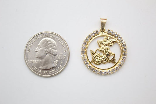 A gold Saint George pendant set with cubic zirconia stones lies next to a US quarter coin to show scale.