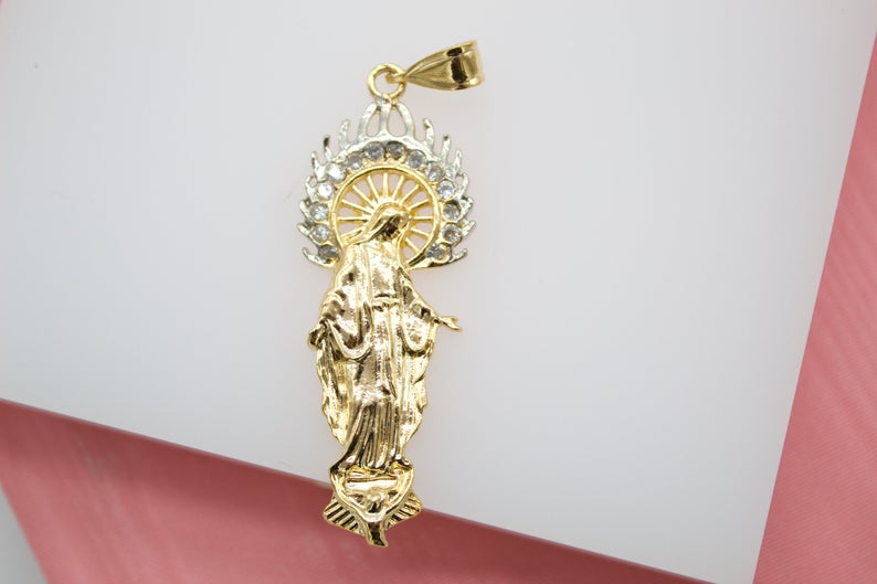 A gold Virgin Mary pendant features sparkling cubic zirconia stones haloing her head against a white background.