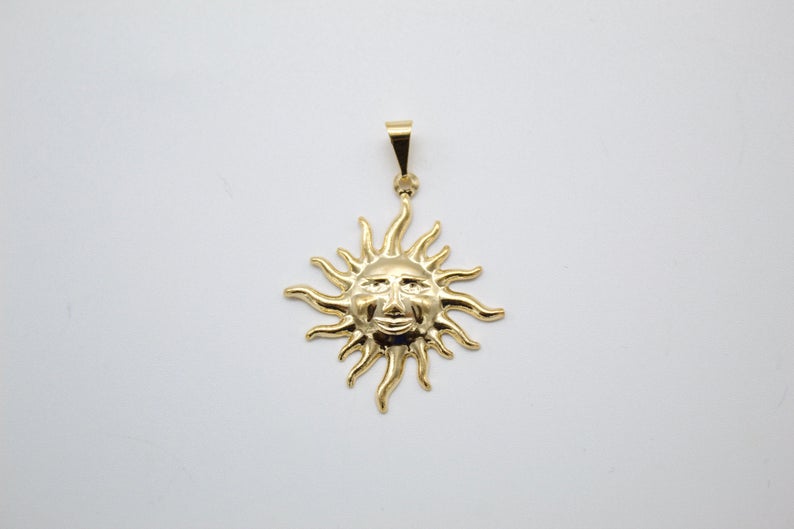A polished gold sun pendant featuring a smiling face and wavy rays hangs against a plain white background.