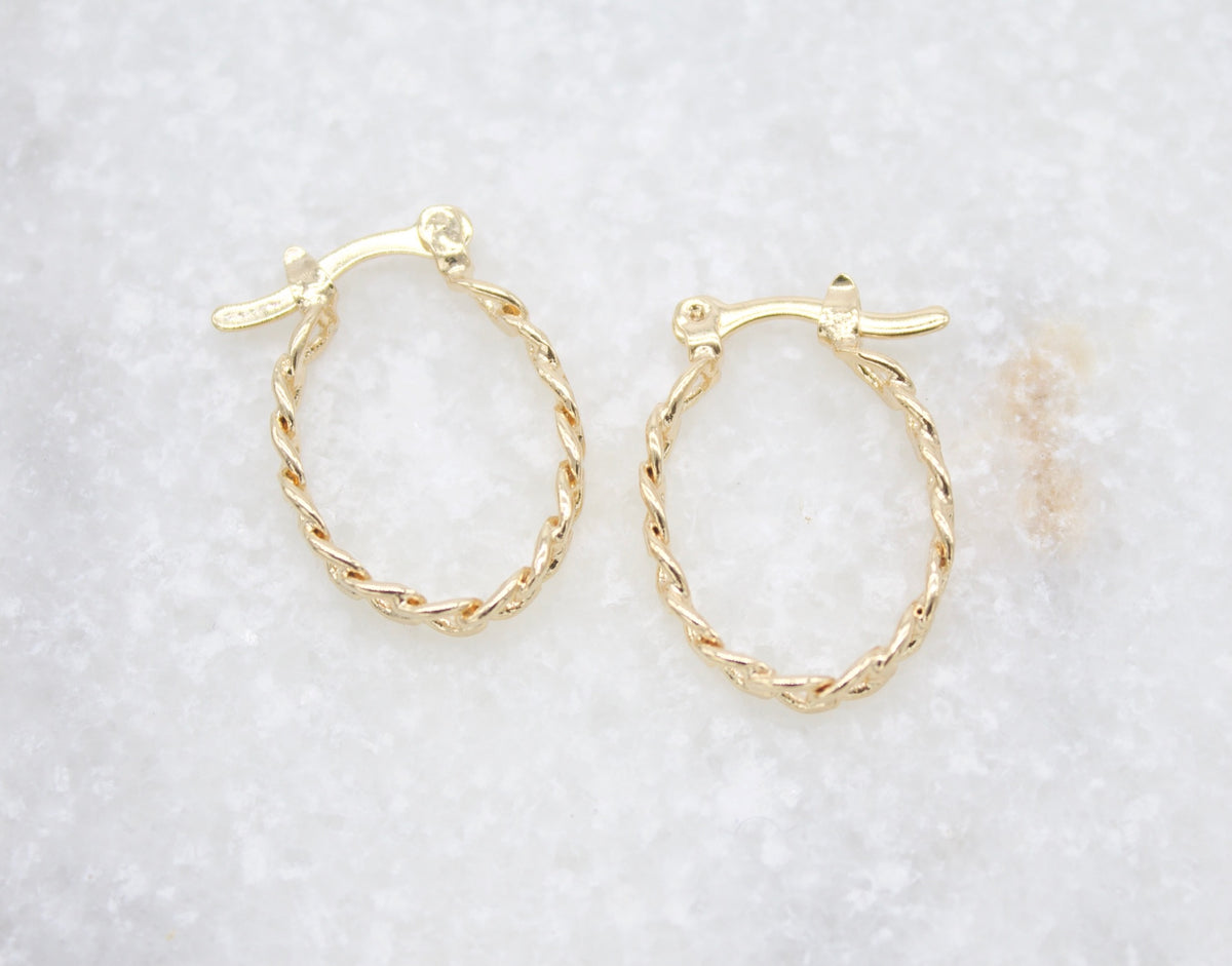 A pair of elegant gold twisted hoop earrings rests on a white marble surface.