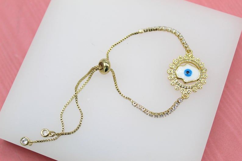 A gold-plated adjustable bolo bracelet sparkles with cubic zirconia stones, featuring a central Hamsa hand pendant with blue and white evil eye enamel details.