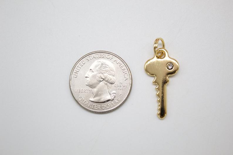A small gold key pendant rests next to a US quarter coin to show scale.