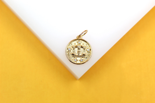 A gold Libra zodiac pendant rests delicately on a white display surface against a vibrant yellow background.