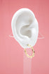 A white mannequin ear displays a shiny gold chain link hoop earring against a pink background.