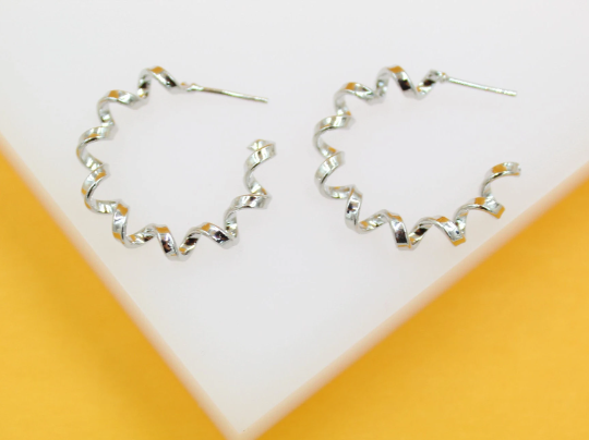 A pair of glossy silver spiral hoop earrings rests on a white display stand against a vibrant yellow background.