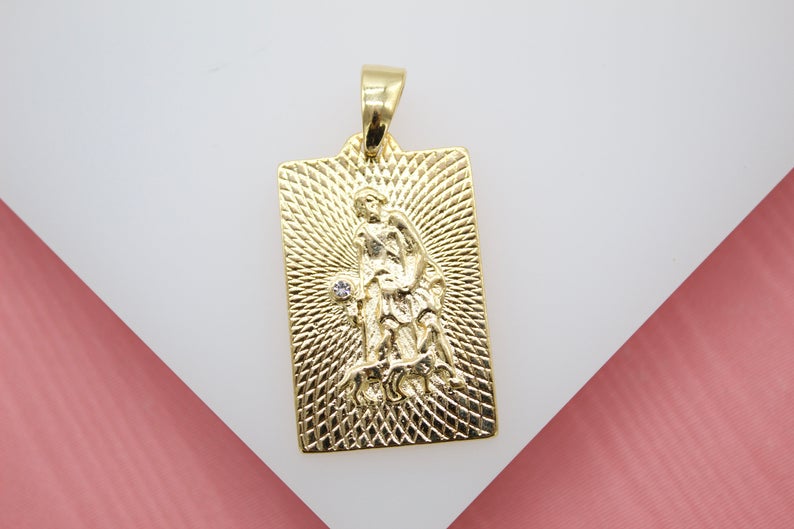 A rectangular gold pendant features a textured engraving of Saint Christopher carrying a child against a sunburst background.