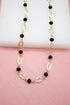 A chic gold-link necklace features alternating textured oval links and faceted black crystal beads against a soft pink and white background.