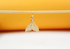 A gold whale tail pendant encrusted with sparkling cubic zirconia crystals hangs from a delicate stick against a warm yellow and white background.