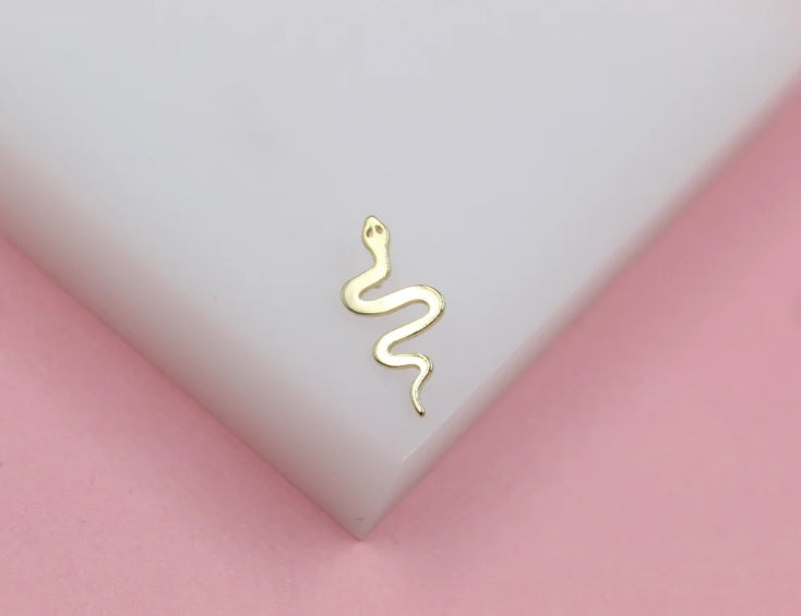 A delicate gold snake earring rests on a white display surface against a pink background.