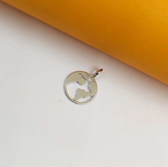 A polished silver world map pendant rests on a white and yellow surface.