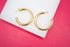 A pair of thick gold hoop earrings rests on a white display block against a vibrant pink background.