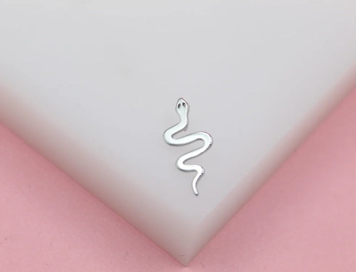 A sleek silver snake stud earring rests on a white display surface against a soft pink background.