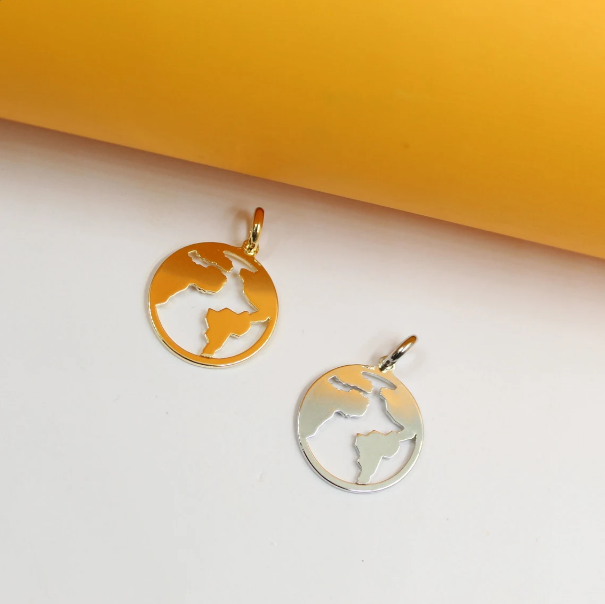 A gold-plated map of the world pendant rests beside a matching silver globe charm against a bright yellow and white background.