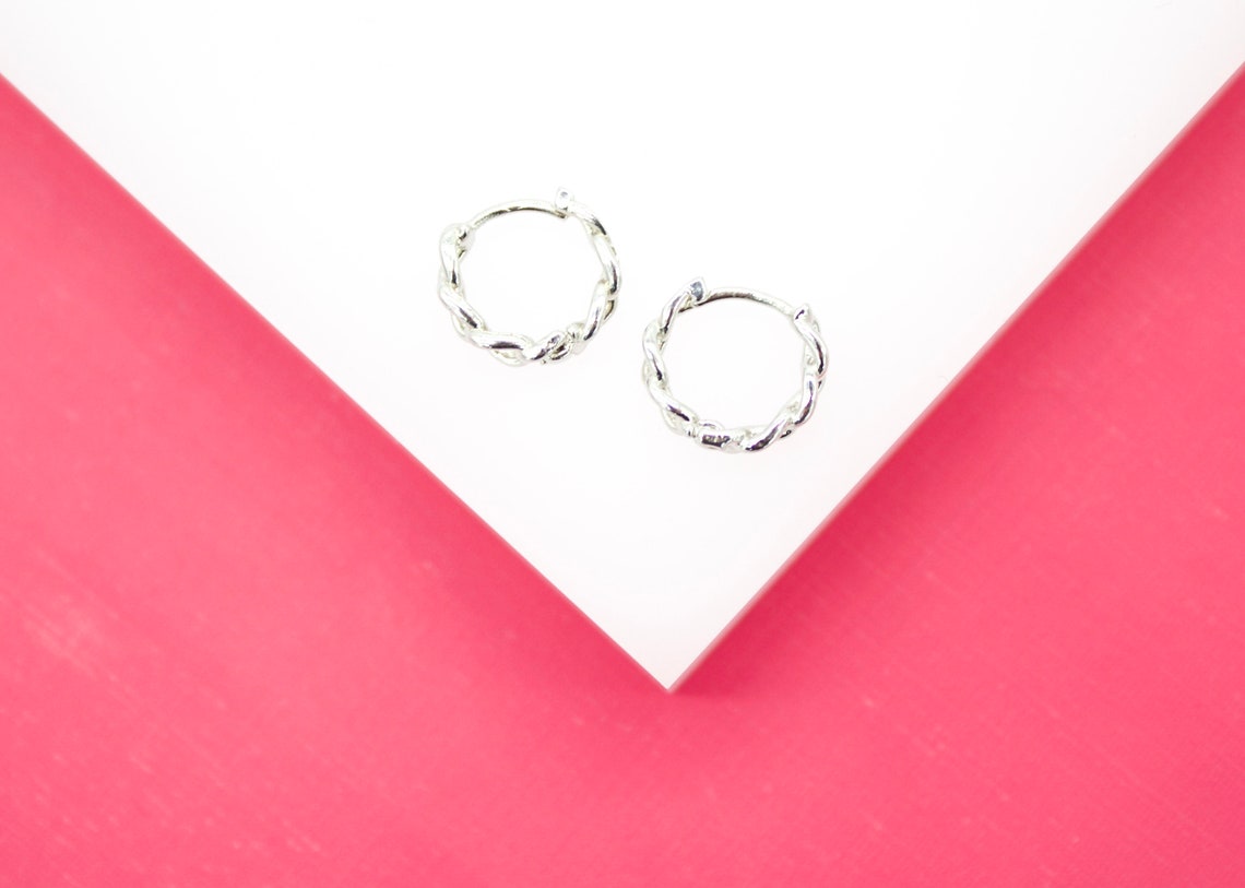 A pair of polished silver twist hoop earrings rests on a white and pink geometric display.