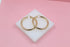A pair of polished gold hoop earrings rests on a small white display block against a soft pink background.
