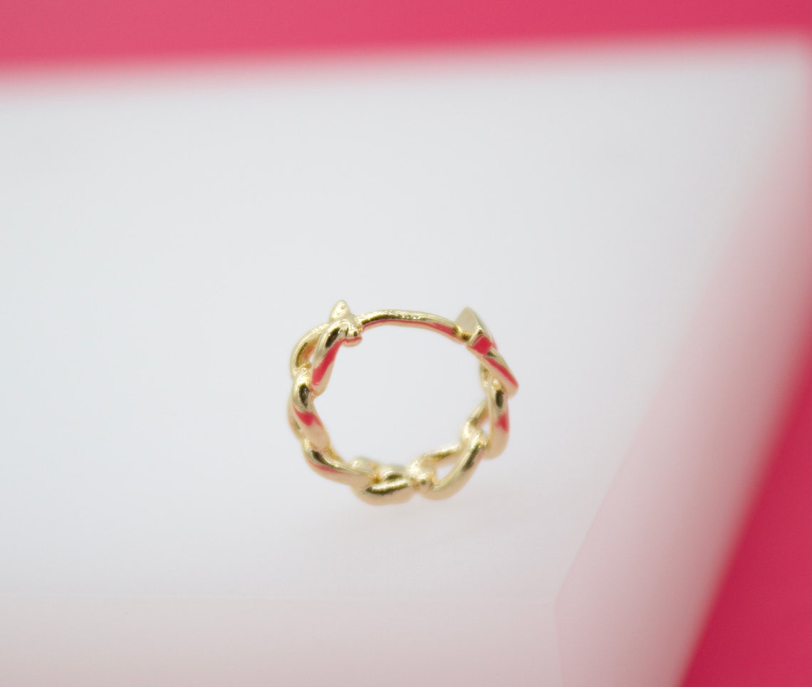 A gold huggie hoop earring features a twisted design accented with vibrant pink enamel.