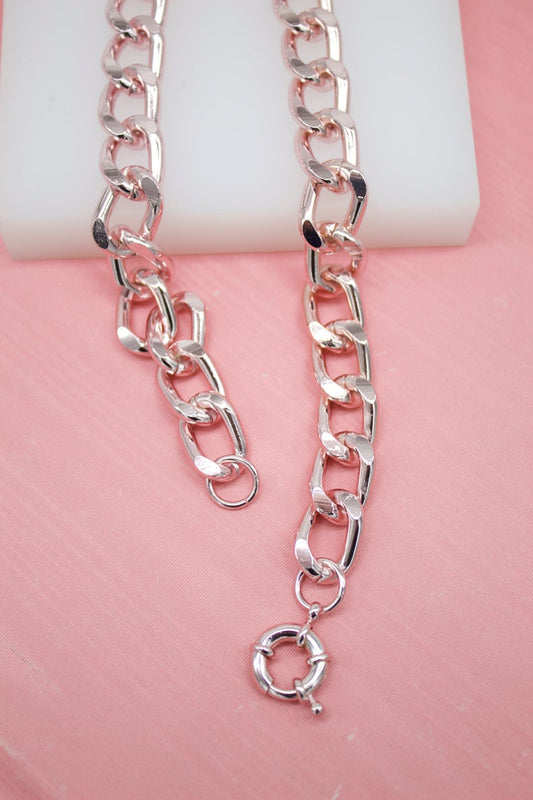 A polished rose gold chain necklace rests on a pink surface with a spring-ring clasp visible.