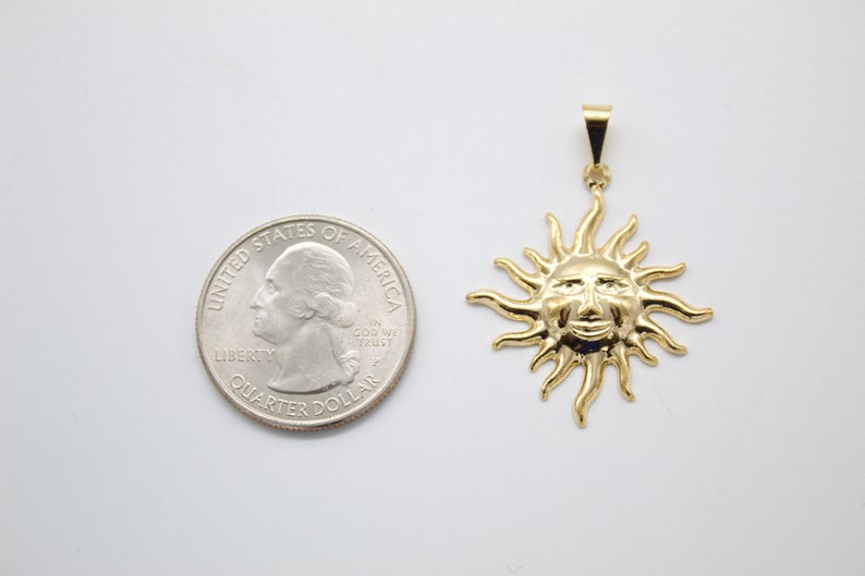 A gold celestial sun face pendant sits beside a US quarter for size comparison on a white surface.