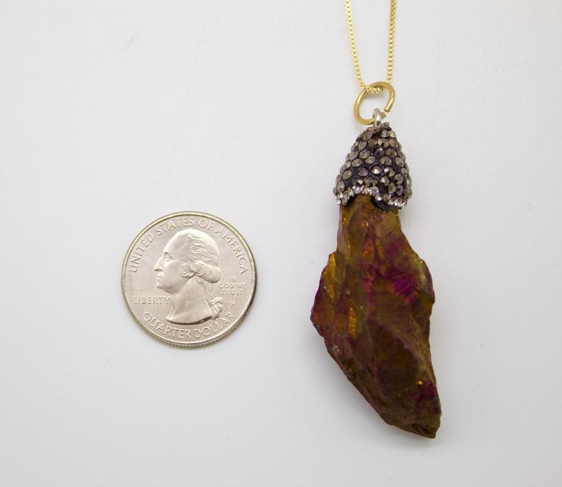 A raw iridescent pyrite crystal pendant hangs from a gold chain next to a US quarter for scale.
