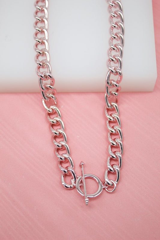 A thick rose gold chunky chain necklace displays a secure toggle clasp against a soft pink background.