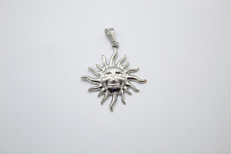 A silver sun pendant features a smiling face with wavy rays against a plain white background.