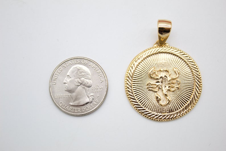 A round gold Scorpio zodiac pendant rests next to a US quarter coin to show its size.