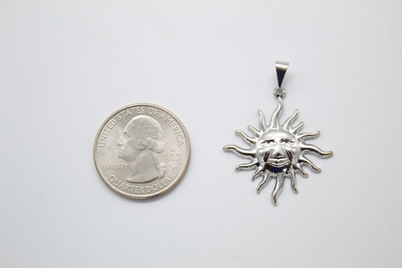 A shiny silver sun face pendant rests next to a US quarter coin to show its scale.
