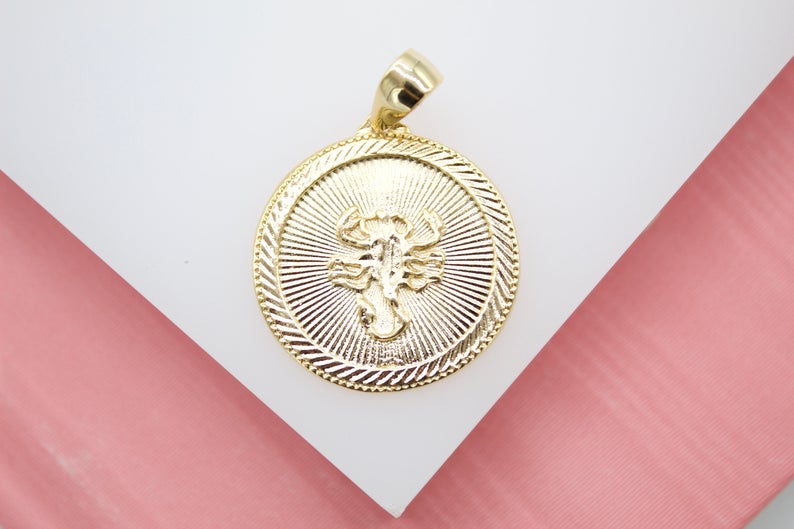 A gold zodiac pendant features an embossed scorpion design on a textured round medal against a light background.