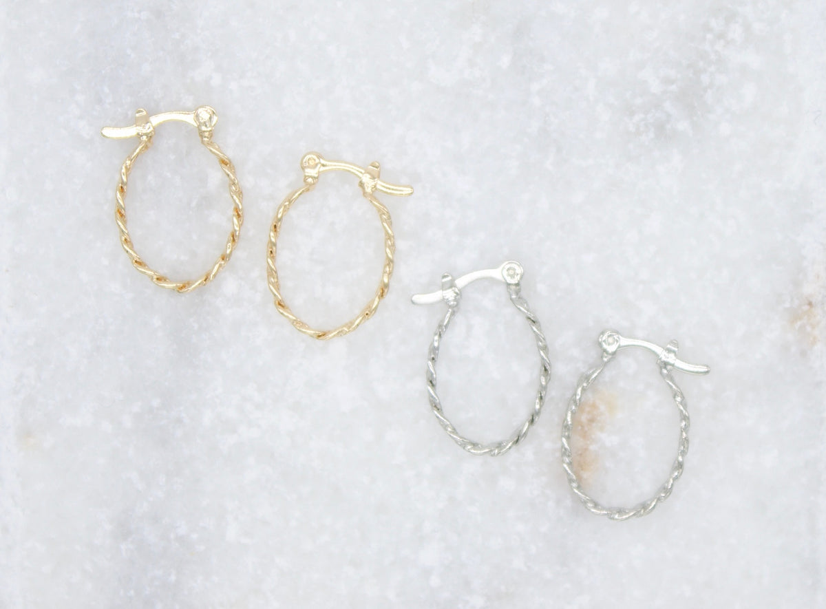 Four small twisted hoop earrings in gold and silver lie diagonally on a white marble surface.