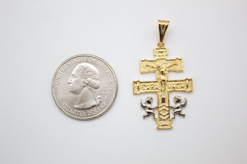 A gold Caravaca cross pendant rests next to a US quarter coin on a white background for size comparison.