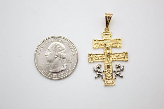 A gold Caravaca cross pendant rests next to a US quarter coin on a white background for size comparison.