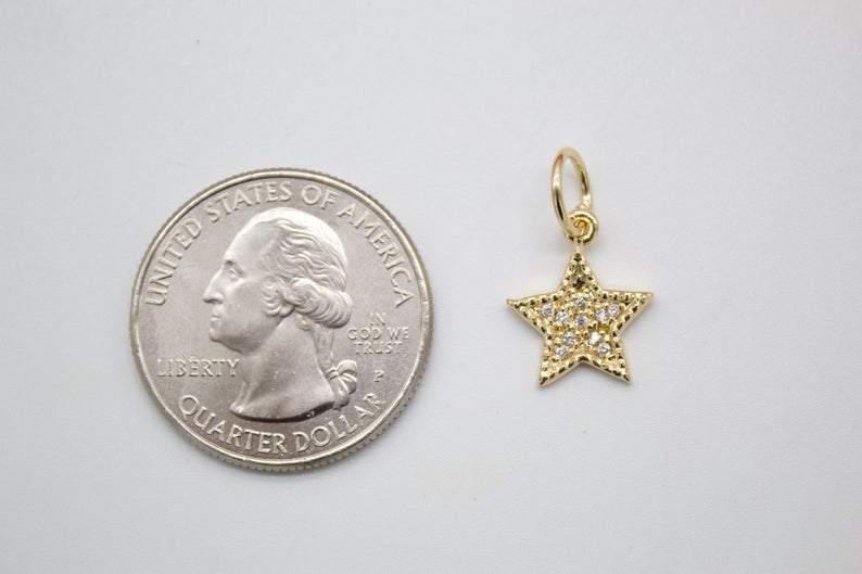 A small gold star pendant with sparkling cubic zirconia stones rests next to a US quarter coin for size comparison.