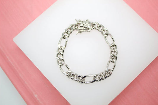 A gleaming silver Figaro link bracelet rests neatly on a white display surface against a pink background.