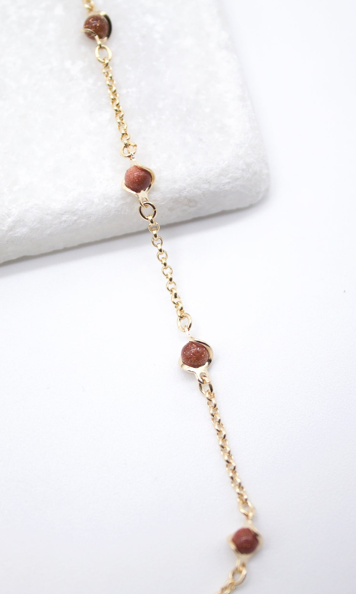 A delicate gold chain bracelet features sparkling brown sandstone bead stations resting on a white surface.