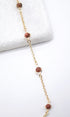 A delicate gold chain bracelet features sparkling brown sandstone bead stations resting on a white surface.