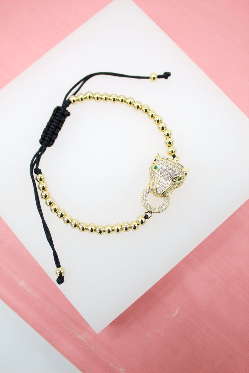 A gold bead slider bracelet features a pave diamond leopard head pendant with green crystal eyes.