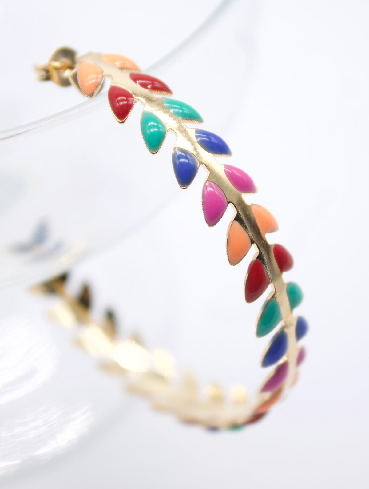 A gold hoop earring features a vibrant pattern of colorful enamel leaves resembling a botanical vine.