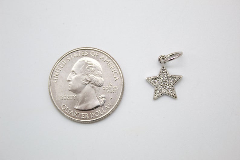 A small pave diamond star charm rests next to a US quarter coin for size comparison on a neutral background.