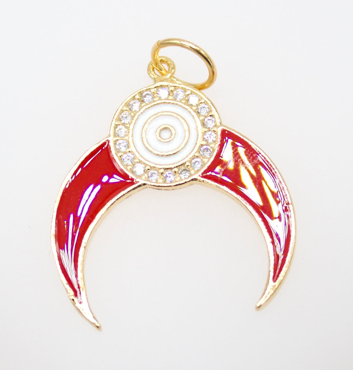 A gold-plated charm features a vibrant red enamel crescent shape accented by a sparkling rhinestone halo and a central white evil eye symbol.