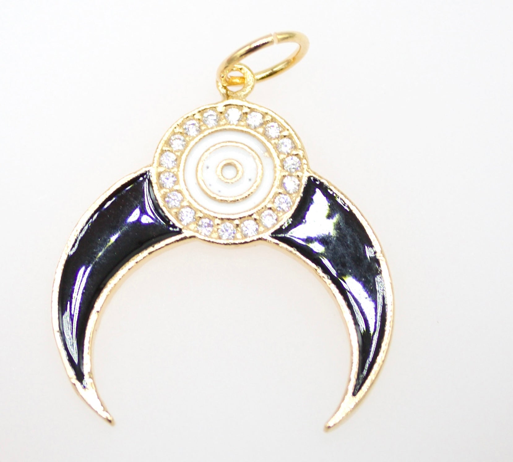 A gold crescent moon pendant features black enamel horns and a central evil eye motif surrounded by sparkling rhinestones.
