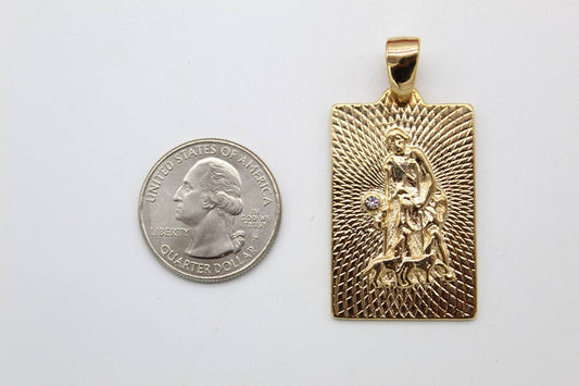 A rectangular gold St. Christopher pendant featuring a textured sunburst background sits next to a US quarter coin for scale.