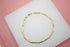 A delicate gold bar link bracelet rests on a white display surface against a pink background.