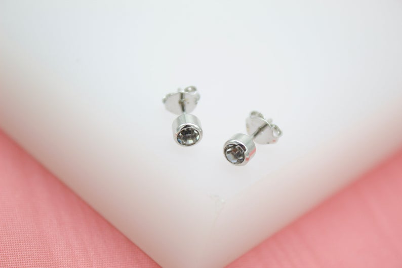 A pair of silver bezel-set crystal stud earrings rests on a white display surface.