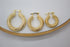 Three graduated sizes of textured gold hoop earrings rest on a white surface within a wooden display tray.