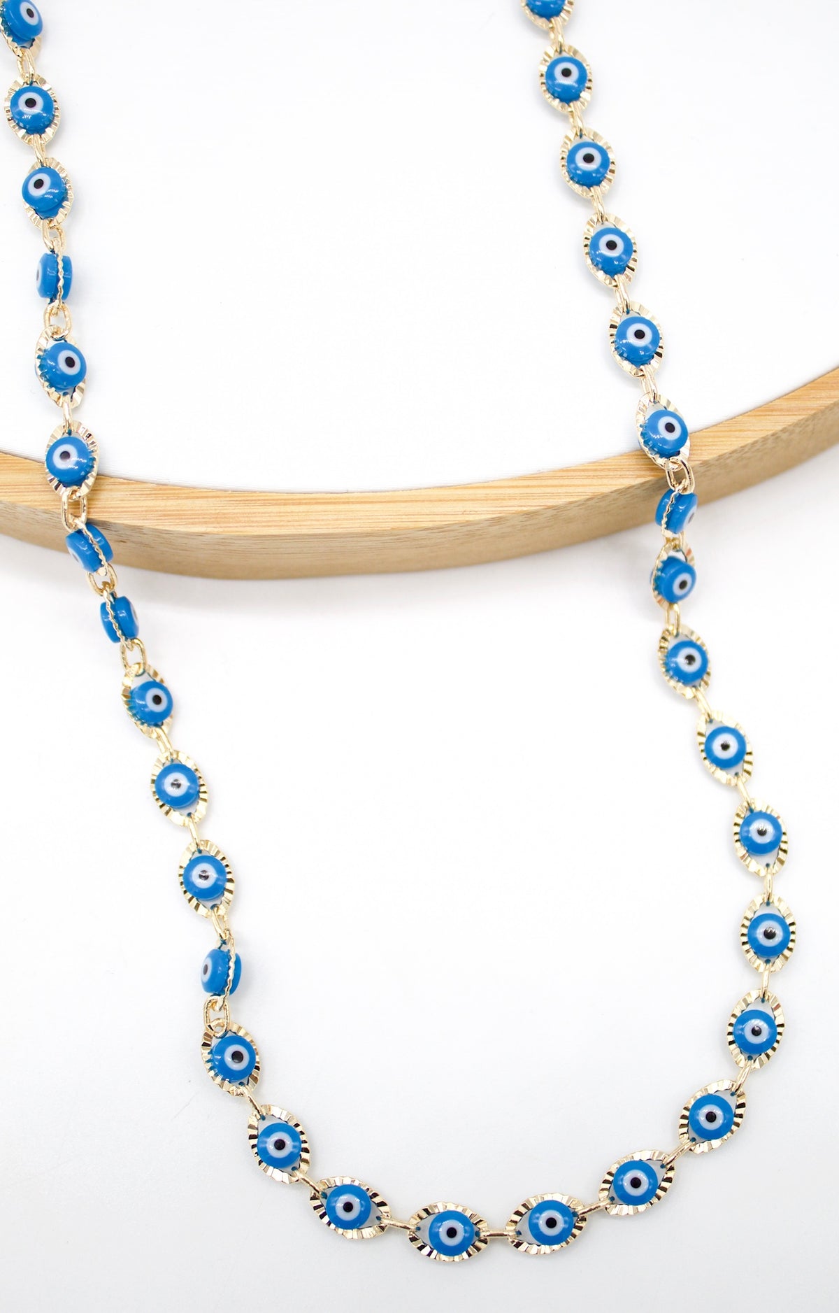 A delicate gold chain featuring alternating blue evil eye beads rests against a neutral white background.